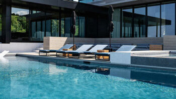 Modern pool with lounge chairs and reflection of a luxury home, showcasing pool filter maintenance.