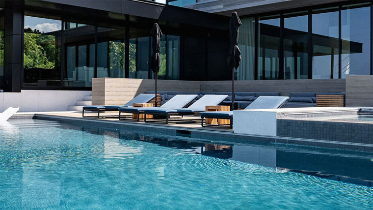 Modern pool with lounge chairs and reflection of a luxury home, showcasing pool filter maintenance.